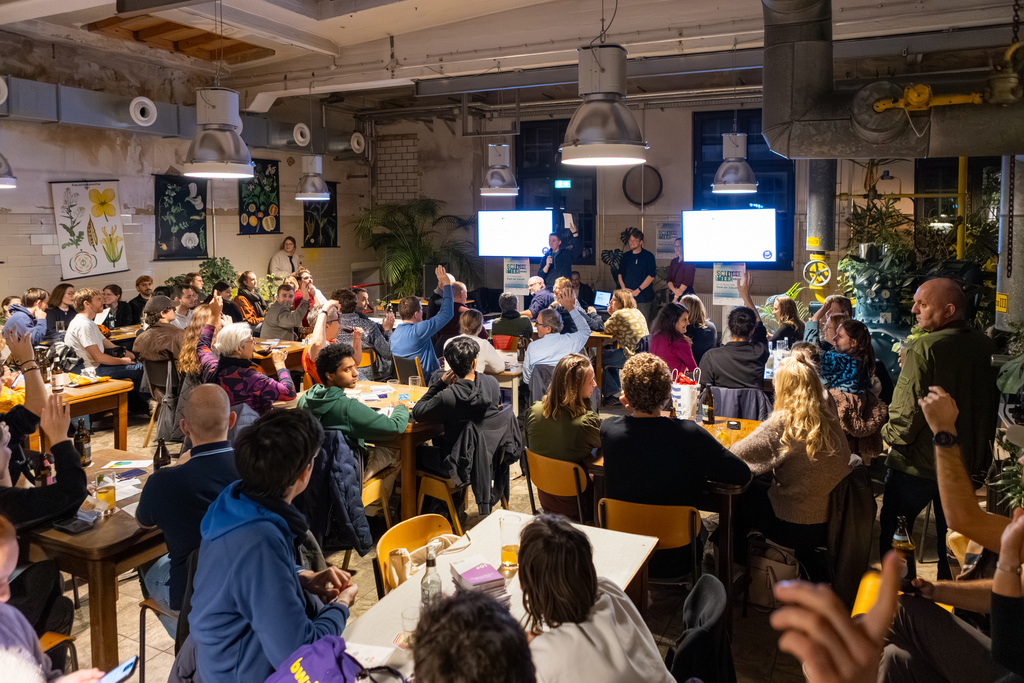 Menschen sitzen in einer gemütlichen Kneipe und lauschen einem Vortrag und stellen Fragen